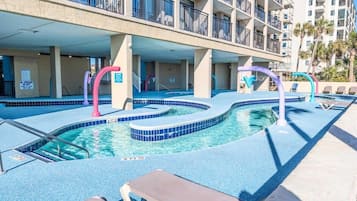 Une piscine au design original, entourée de chaises longues et d’un immeuble à plusieurs étages doté de balcons.
