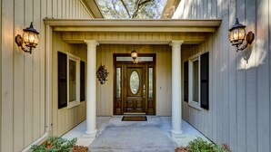 A house entrance with a wooden door, two columns, and two wall-mounted lights.
