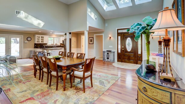 A spacious dining area with a wooden table and chairs, a kitchen in the background, and skylights.