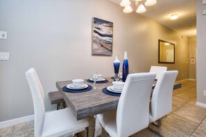 A dining area with a wooden table, white chairs, and a painting on the wall.