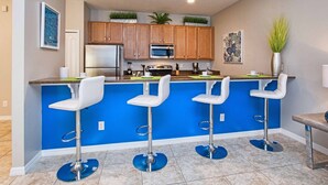 Eine moderne Küche mit blauer Akzentwand, Edelstahlgeräten und drei weißen Barhocker.