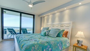 Un dormitorio con una cama grande, una mesita de noche con lámpara, un ventilador de techo y vistas al balcón con sillas.
