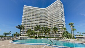 Un hotel moderno con fachada curva, piscina y palmeras.