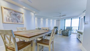 Un comedor amplio con una mesa y sillas de madera, un ventilador de techo y un ventanal que proporciona luz natural.