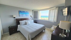 A bedroom with a bed, nightstands, a desk with a lamp, a painting, and a window with blinds. - 🌅Unit #401 –Unobstructed Gulf Views & Dolphin Watching from Your Balcony🌊🐬 (Destin)