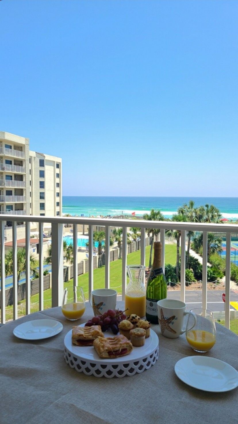A balcony with a table set for breakfast, overlooking a beach and ocean.