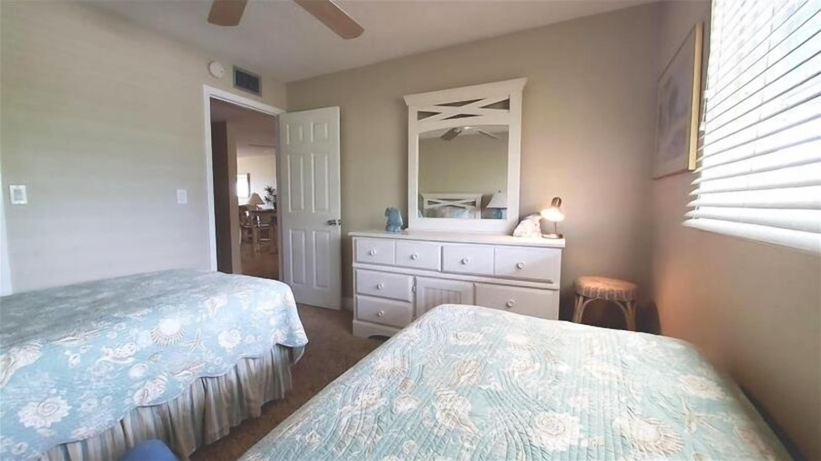A bedroom with two single beds, a dresser, a mirror, and a window with blinds.