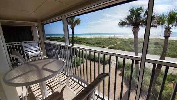 Een balkon met een tafel en stoelen, uitkijkend op een strand met palmbomen en de oceaan.