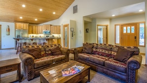 A spacious living area with a wooden ceiling, a kitchen with a bar, and a large brown leather sofa. - CAMA16 - Sharc Passes, AC, Pool and Ping Pong Tables, Hot Tub (Sunriver)