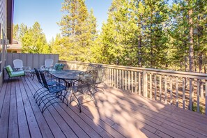 Une terrasse en bois, aménagée avec du mobilier d’extérieur, notamment une table et des chaises, donnant sur une zone boisée.