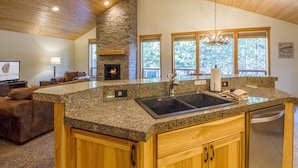 A spacious kitchen with granite countertops, a stone fireplace, and large windows offering views of the outdoors. - CAMA16 - Sharc Passes, AC, Pool and Ping Pong Tables, Hot Tub (Sunriver)