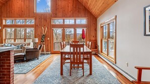 A spacious room with a high ceiling, wooden walls, and large windows offering views of the outdoors. - Treetops: 4 br, woodstove, a/c, deck & views, firepit, garage, great location! (Stowe)