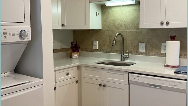 A modern kitchen with white cabinets, a dishwasher, a sink, and a countertop with a paper towel holder.