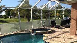 A clear swimming pool with a tiled edge, a built-in waterfall feature, and a covered patio area with lounge chairs and a barbecue grill. - "Luxury Villa in Punta Gorda, FL - 4BD/3BA, Pool, Jacuzzi" Sandhill Cranes. (Punta Gorda)