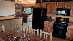 Una cocina rústica con armarios de madera, un refrigerador negro, una estufa y un comedor con una mesa y sillas de madera.