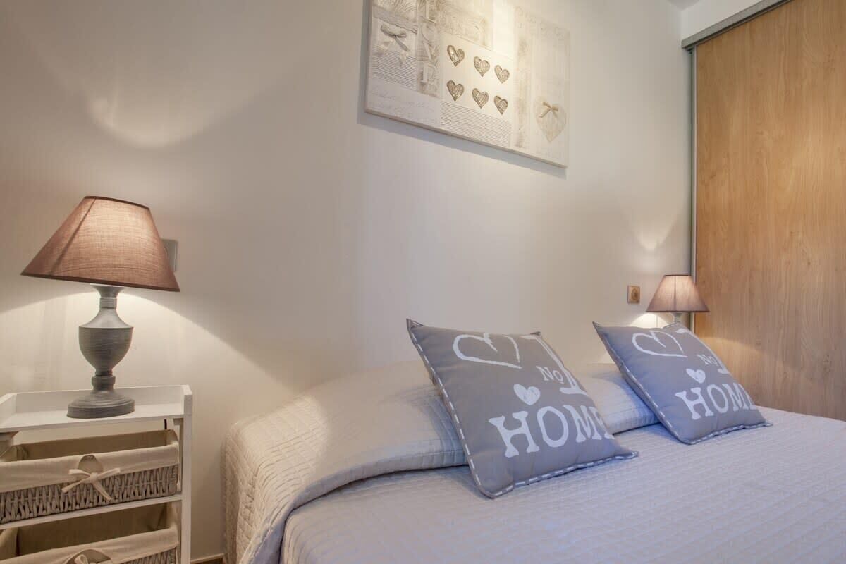 A bedroom with a bed, two pillows with 'I ♥ HOME' text, a lamp, and a wall art piece.