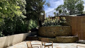 An outdoor patio with stone flooring, wooden furniture, and a stone wall. - Domaine Ghjulia - Casa Nebbiu (Patrimonio)
