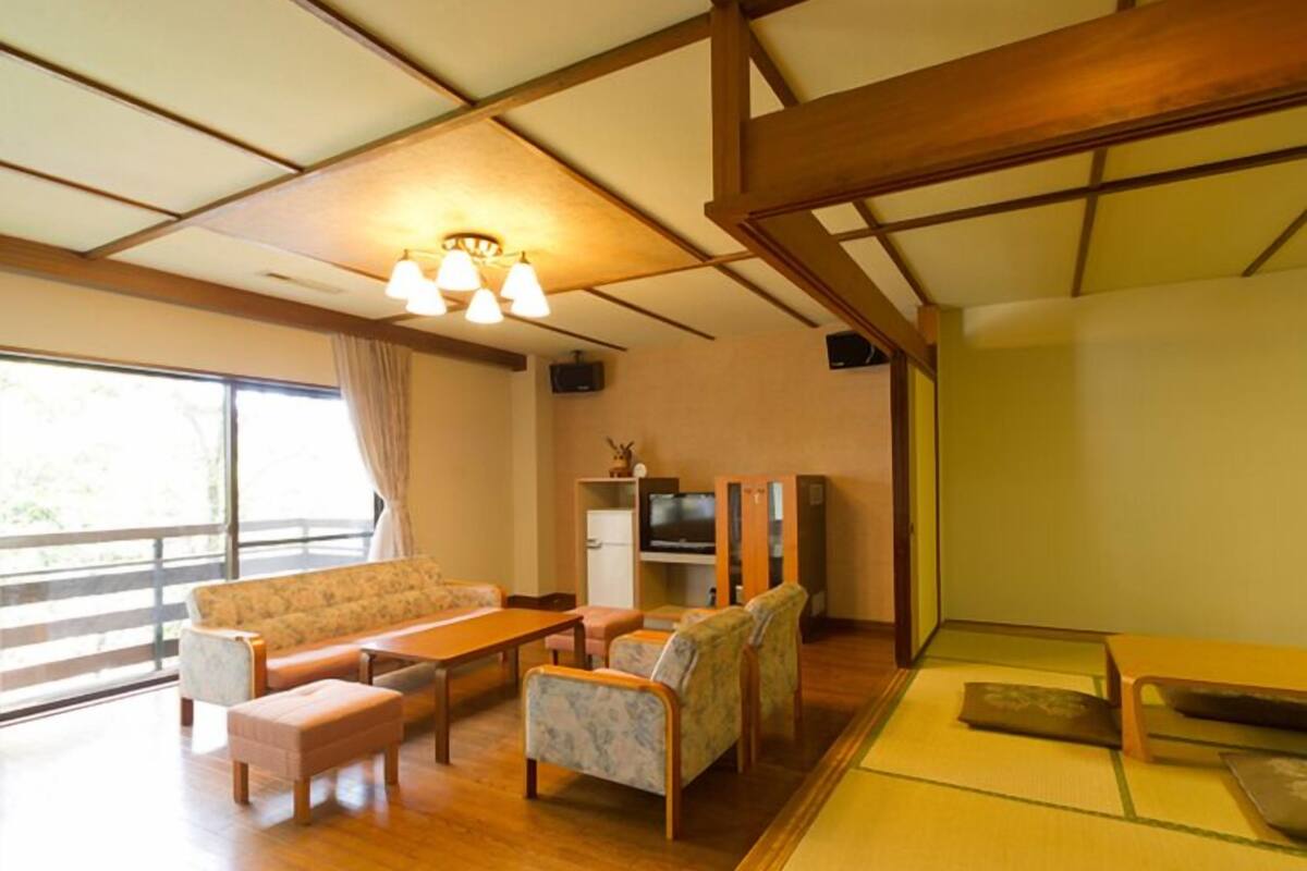 A room with a sofa, chairs, a table, a TV, and a wooden ceiling structure.