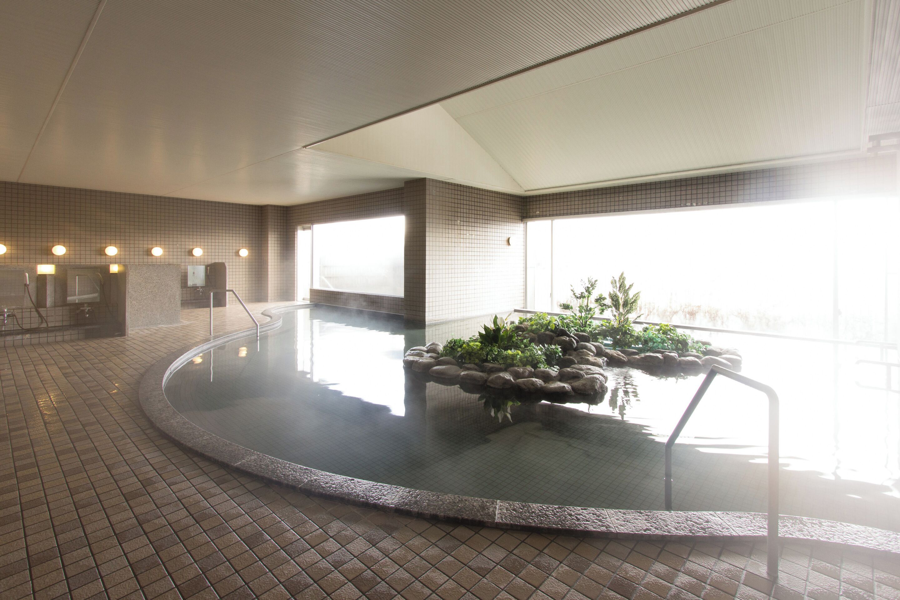 A hot tub area with tiled flooring, a stone edge, and a plant arrangement.