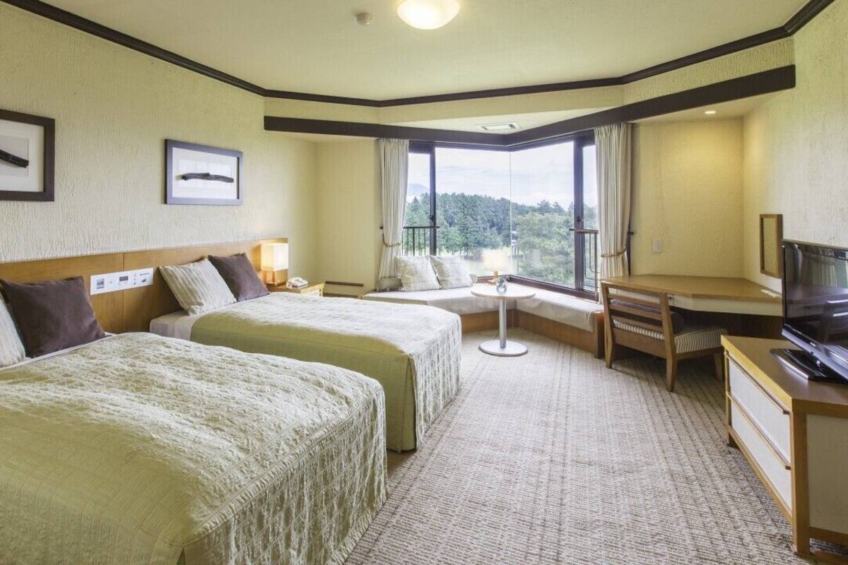 A hotel room with two beds, a desk, a television, and a window with a view.