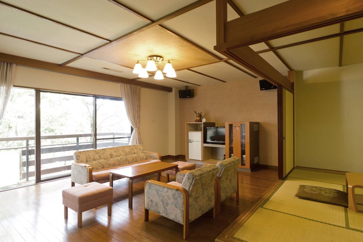 A traditional Japanese-style living room with tatami flooring, a low wooden table, a sofa, and a television set.