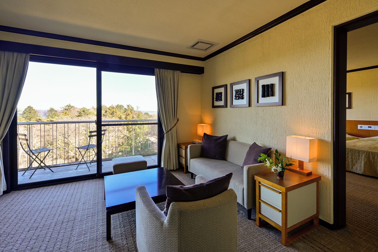 Una habitación de hotel con balcón, sofá, mesa y lámpara.