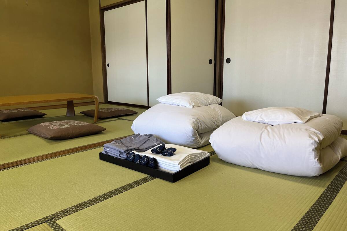 A traditional Japanese room with tatami flooring, a low wooden table, and a bed with white bedding and pillows.