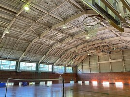 Un centro deportivo interior con techos altos, aros de baloncesto y una red de voleibol.