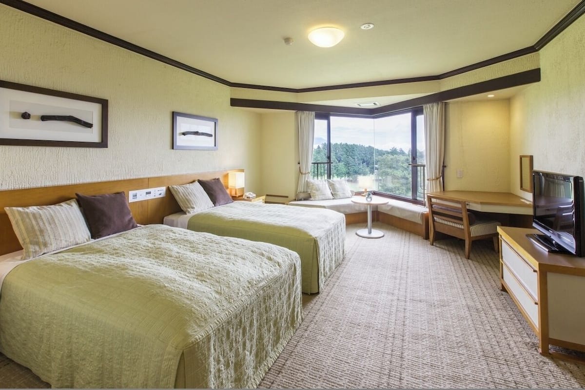 A hotel room with two beds, a desk, a TV, and a balcony with a view.