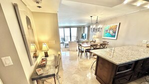 A modern kitchen with a large island, a dining area with a table and chairs, and a living space with a sofa and a TV. - Gorgeous beach views! Private sun deck! 4133 BS1 (Miramar Beach)