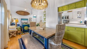 A compact kitchen with green cabinets, a wooden dining table, wicker chairs, and a hanging light fixture. - AM I Dreaming: Heated Pool, Family Friendly Home, 3-min walk to beach! (Holmes Beach)