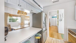 A modern kitchen with a central island, stainless steel appliances, and a view into the dining area. - AM I Dreaming: Heated Pool, Family Friendly Home, 3-min walk to beach! (Holmes Beach)