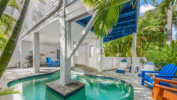 An indoor swimming pool with a clear blue water feature, surrounded by blue and orange Adirondack chairs, and a covered seating area with a white ceiling and walls. - AM I Dreaming: Heated Pool, Family Friendly Home, 3-min walk to beach! (Holmes Beach)