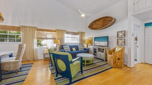 A spacious living area with a large window, a ceiling fan, and a dining table with chairs. - AM I Dreaming: Heated Pool, Family Friendly Home, 3-min walk to beach! (Holmes Beach)
