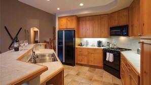 Una cocina con armarios de madera, un refrigerador de acero inoxidable, un microondas, una estufa y un lavamanos.