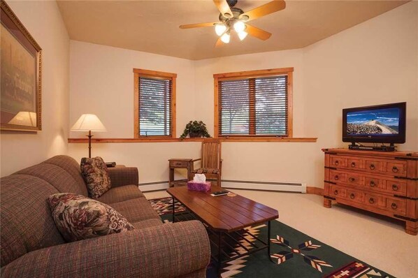 A living room with a sofa, a coffee table, a TV, and a ceiling fan.