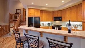 Una cocina con gabinetes de madera, un refrigerador, un microondas y una barra con taburetes.