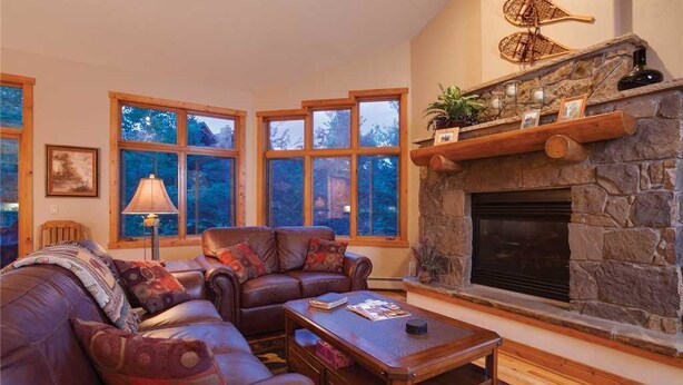 Una sala de estar acogedora con chimenea de piedra, sofá de cuero y ventanas amplias.