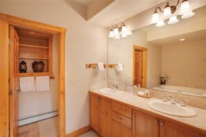 A bathroom with wooden cabinets, two sinks, a large mirror, and a light fixture above the mirror.