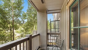 A balcony with a wooden railing, two metal chairs, and a view of trees and a building. - River Run Condo has Private Balcony w/ Mountain Views, Close to Shops/Dining! (Keystone)