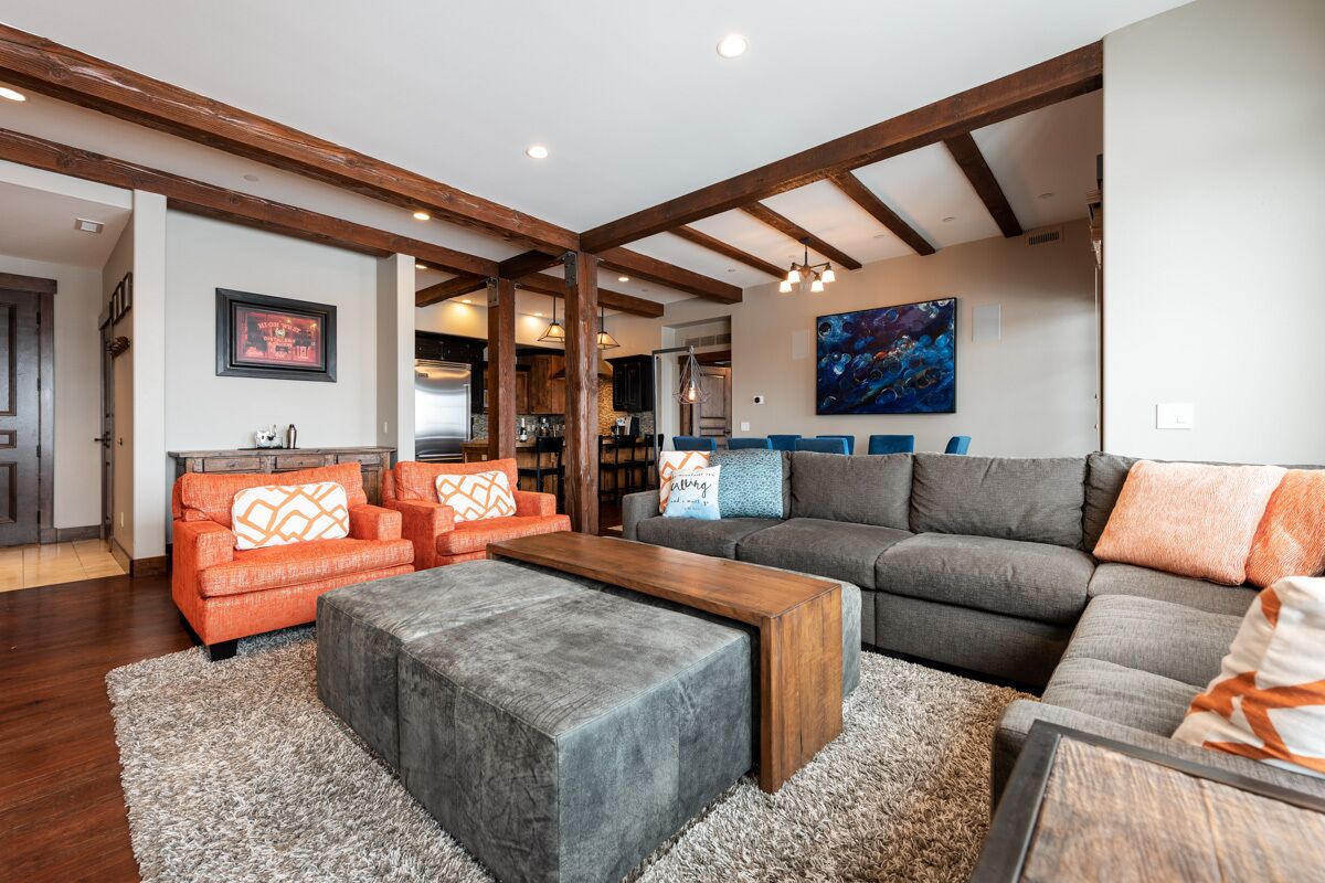 Uma sala de estar ampla com um sofá seccional cinza, poltronas laranjas e uma mesa de centro de madeira.