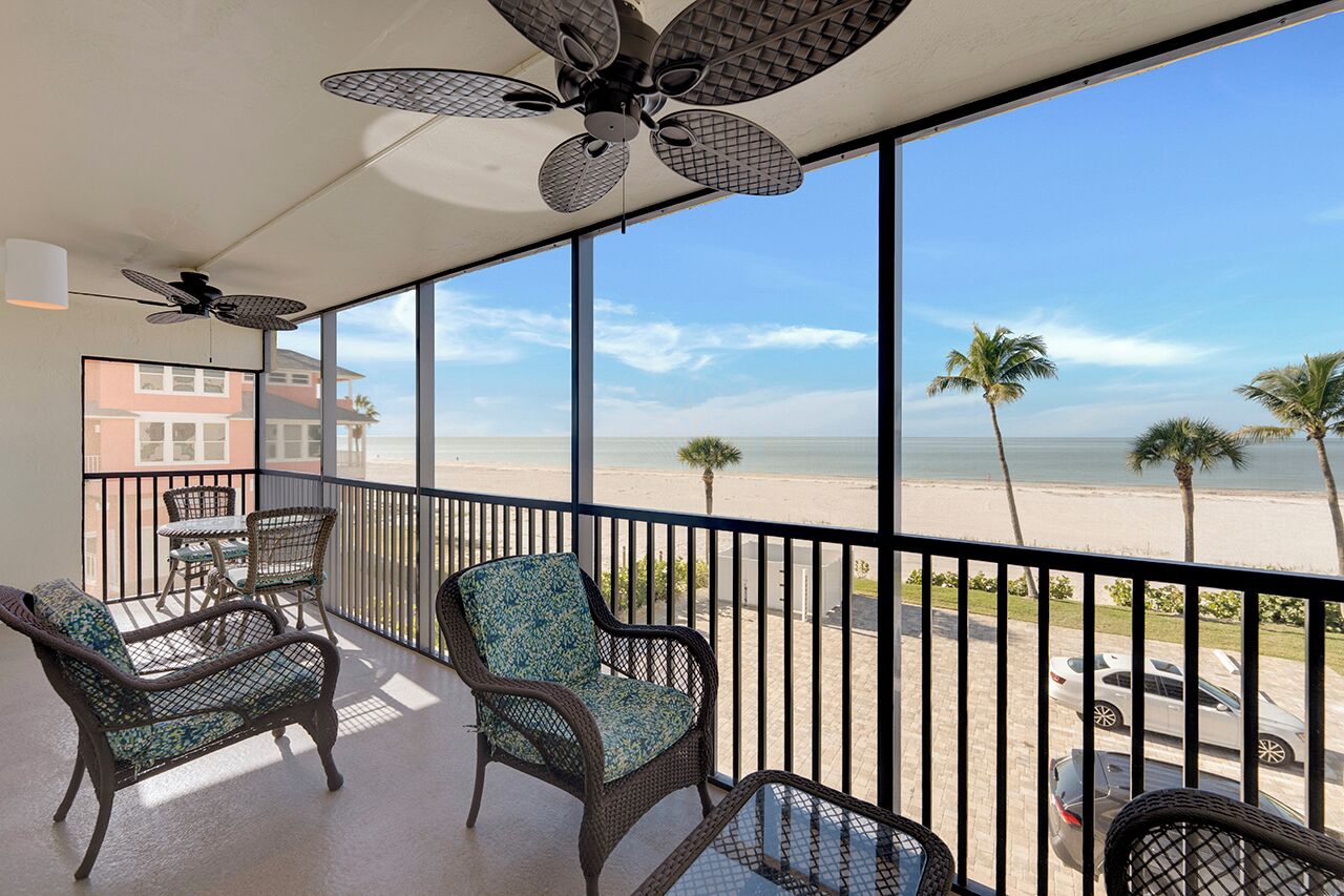 A balcony with wicker furniture, a ceiling fan, and a view of the beach.