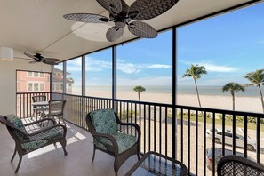 A balcony with wicker furniture, a ceiling fan, and a view of the beach.