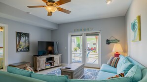 Un salon avec un canapé de couleur turquoise, une table basse en bois, un téléviseur et un ventilateur de plafond.