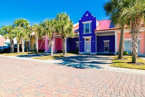 A row of colorful houses with a paved driveway and palm trees.