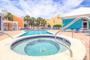 A swimming pool with a hot tub, surrounded by lounge chairs and a white fence.
