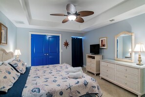 A bedroom with a bed, a dresser, a television, and a ceiling fan.