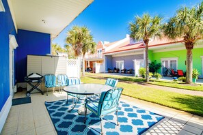 An outdoor patio with a round table and chairs, a blue patterned rug, and a white umbrella.