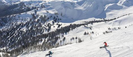 A snowy mountain landscape with ski slopes, trees, and distant mountains.