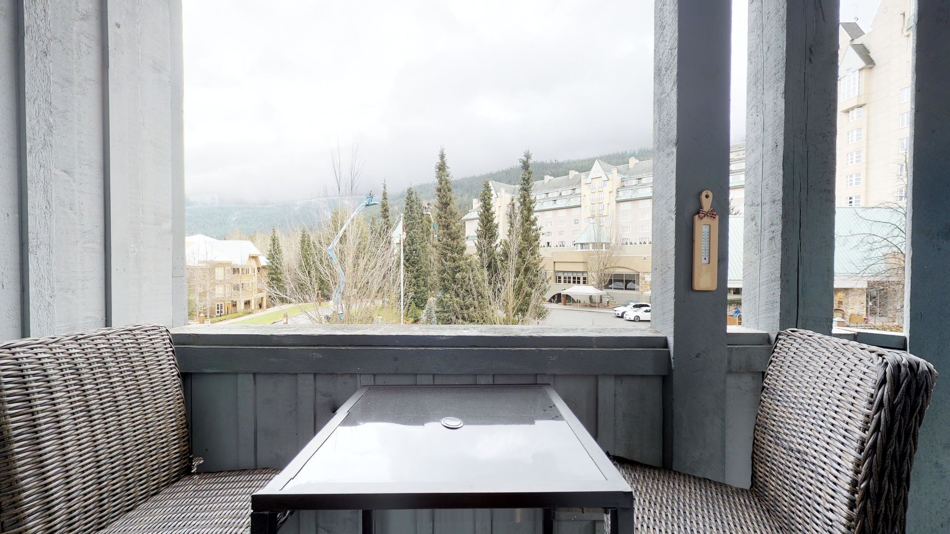 A balcony with wicker furniture, a table, and a view of buildings and trees.